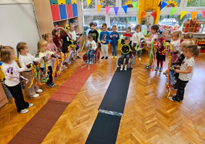 zabawa wyścigi - chłopcy siedzą na krzesełkach, poruszają nogami aby droga - bibuła została wciągnięta pod krzesełko, dziewczynki dopingują