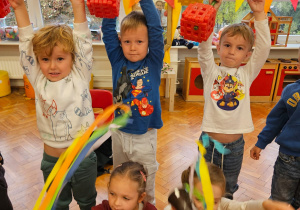 chłopcy podnoszą sztangi wykonane z klocków a dziewczynki machają kolorowymi bibułkami dopingując ich