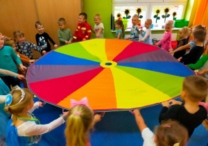 przedszkolaki w sali w czasie zabaw z chustą animacyjną krążą w kole