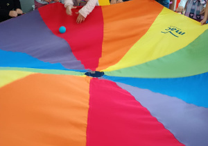 przedszkolaki w sali w czasie zabaw z chustą animacyjną próbują skierować piłeczkę do otworu