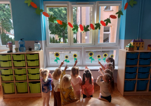 przedszkolaki pokazują swoją jesienną girlandę zawieszoną na oknie