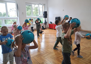 dzieci trzymają piłki nad głowami i maszerują po sali