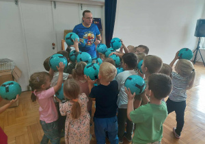 dzieci stoją z piłkami uniesionymi w górę przy trenerze