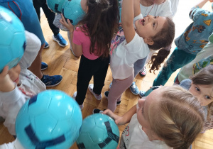 dzieci stoją z piłkami uniesionymi w górę przy trenerze