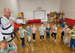 przedszkolaki ćwiczą z trenerem wyrzuty ramion przed siebie