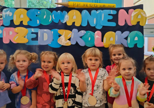 zdjęcie grupowe dziewczynek przed tablicą z napisem pasowanie na przedszkolaka