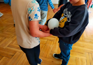 dzieci trzymają się za ręce a piłka leży na nich
