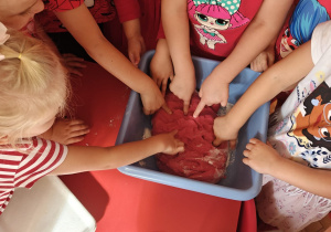 dzieci ubrane na czerwono ugniatają czerwoną masę