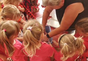 dzieci ubrane na czerwono obserwują nauczycielkę ugniatającą czerwoną masę