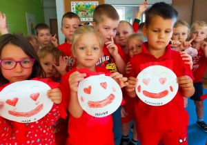 przedszkolaki ubrane na czerwono trzymają uśmiechnięte buźki