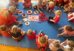 dzieci z nauczycielką siedzą w kole wokół czerwonych przedmiotów