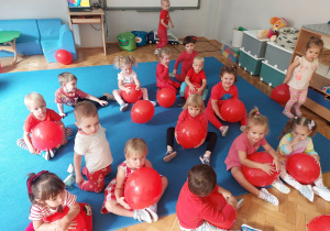 przedszkolaki siedzą z czerwonymi balonami na macie