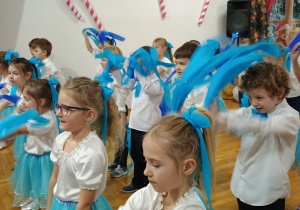 dzieci tańczą w szeregach z niebieskimi wstążkami