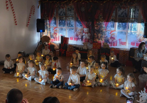 przedszkolaki śpiewają i trzymaja w rękach lampki przy zgaszonym świetle