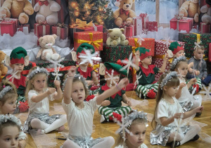 przedszkolaki siedzą w rzędach i podnoszą do góry śnieżynki umieszczone na patyczkach