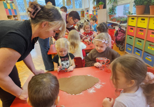 mama wałkuje ciasto na pierniczki na stoliku, przy którym siedzą dzieci