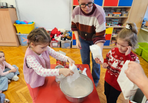 dziewczynki wspują do miski gotową msę piernikową pod okiem mamy