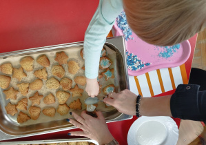dziecko obsypuje pierniczki kolorowymi dodatkami