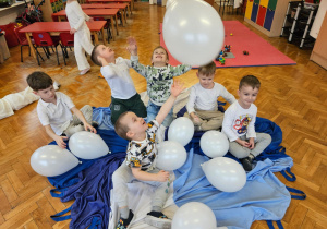chłopcy bawią się białymi balonami na biało - niebieskiej chustce