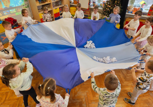 przedszkolaki poruszają chustą animacyjną, na której podskakują papierowe kulki