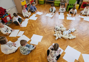 przedszkolaki siedzą w kole z białymi kartkami papieru
