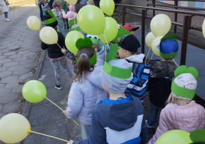 dzieci z zielonymi balonami w korowodzie przed budynkiem przedszkola