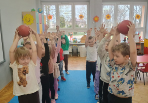 dzieci podają sobie piłkę rąk do rąk stojąc w rzędach, jeden za drugim