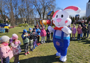 Zając Wilekanocny wita się z dziećmi stojącymi w ogrodzie