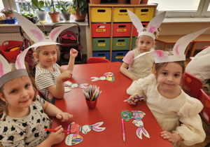 dzieczynki w opaskach z uszami zajęczymi ozdabiają zajączki tekturowe