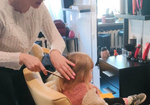 fryzjerka czesze dziewczynkę, która siedzi na fotelu przed lustrem