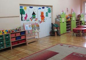 sala dla młodszych dzieci z zielonymi szafkami wykończonymi 3 żabkami przy drzwiach do sali zabaw