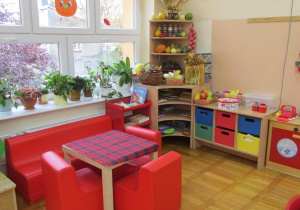 sala, kącik relaksacyjny z czerwoną kanapą,, fotelami i stolikiem oraz grami